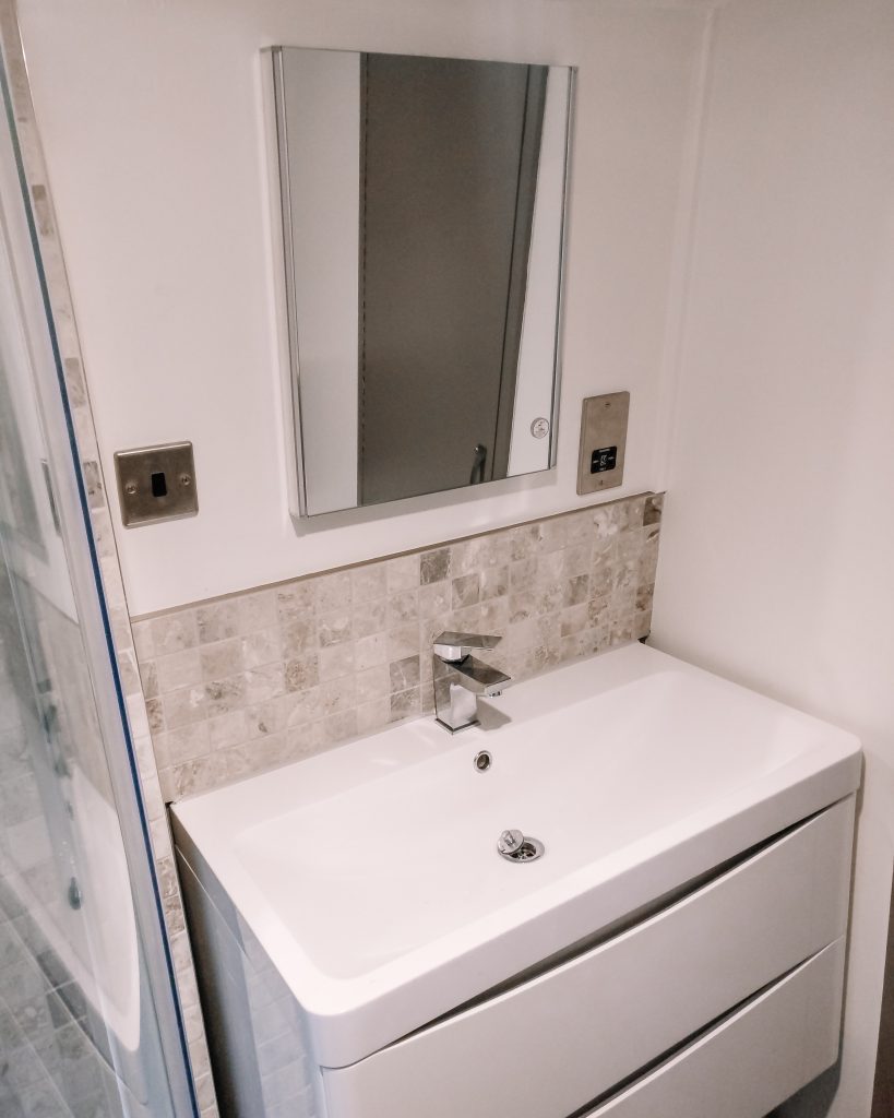 White wall hung vanity unit with LED mirror and travertine splashback
